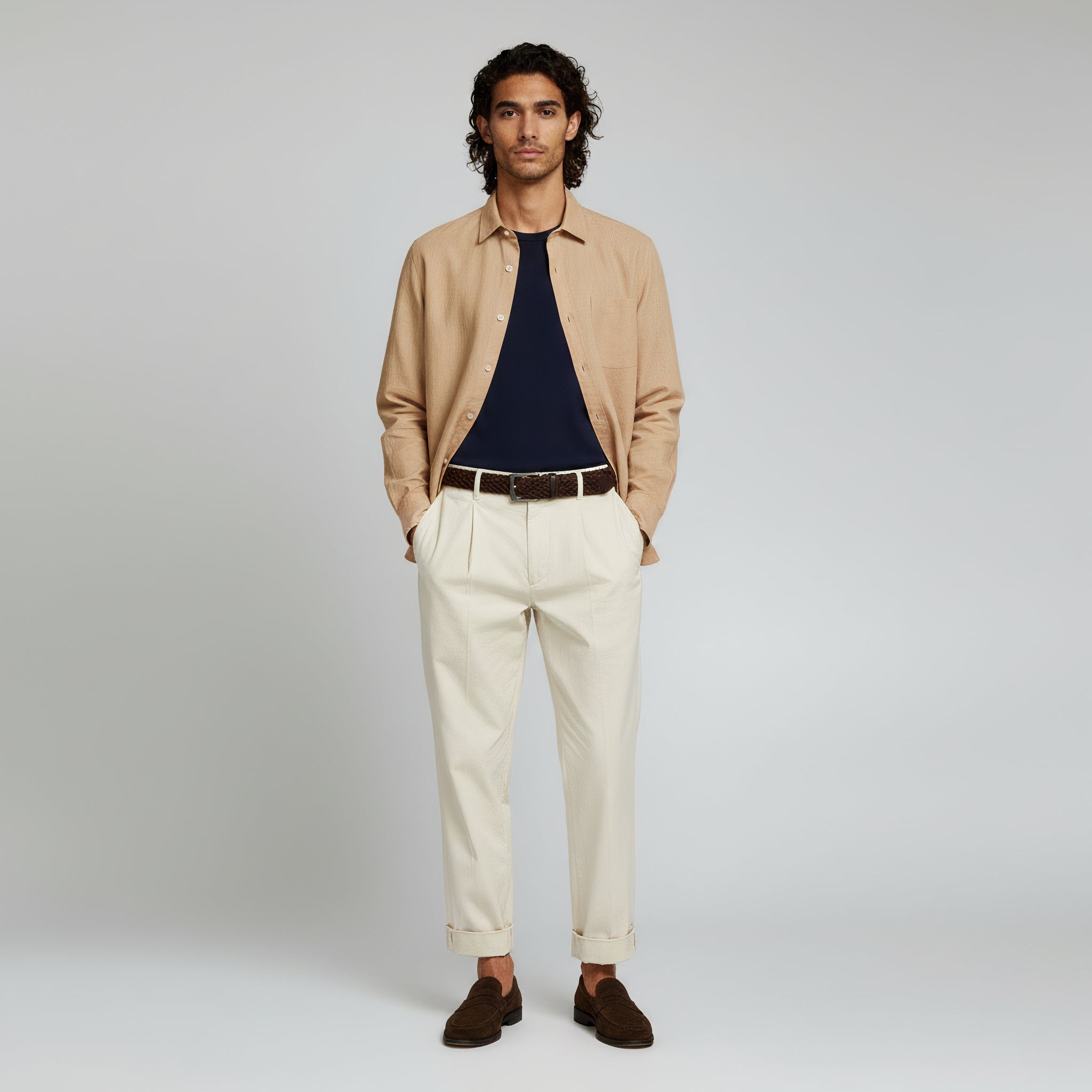 man wearing black inner shirt and brown long sleeve polo and beige trousers on a plain background