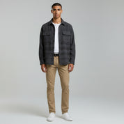 man wearing white inner t-shirt with jacket paired with khaki jeans and white shoes on a plain background