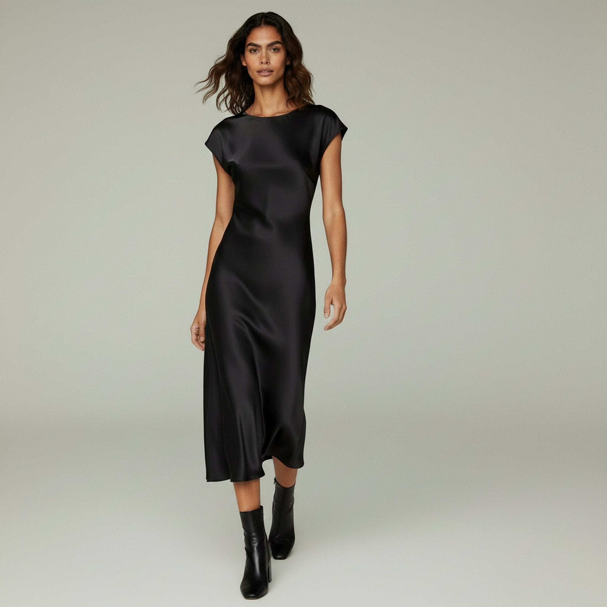 woman wearing black midi dress paired with black boots on a plain backgorund