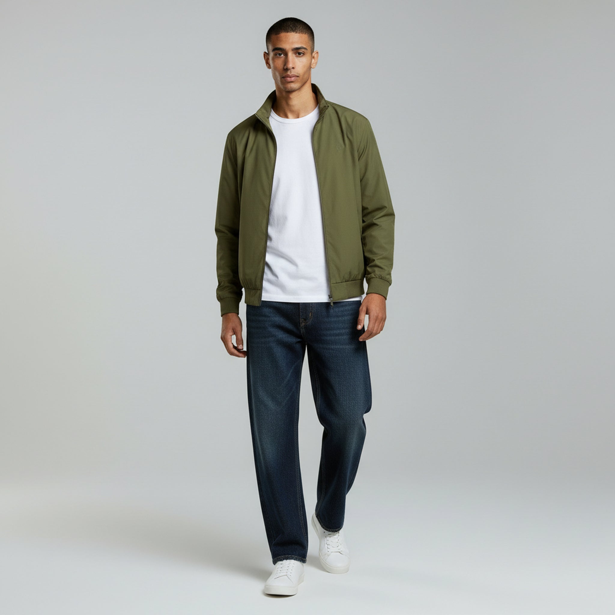 man in white shirt with green jacket and black jeans on a plan background