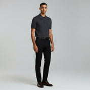 man wearing dark grey polo shirt and black pants on a plain background