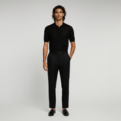 man wearing black polo shirt and black trousers on a plain background