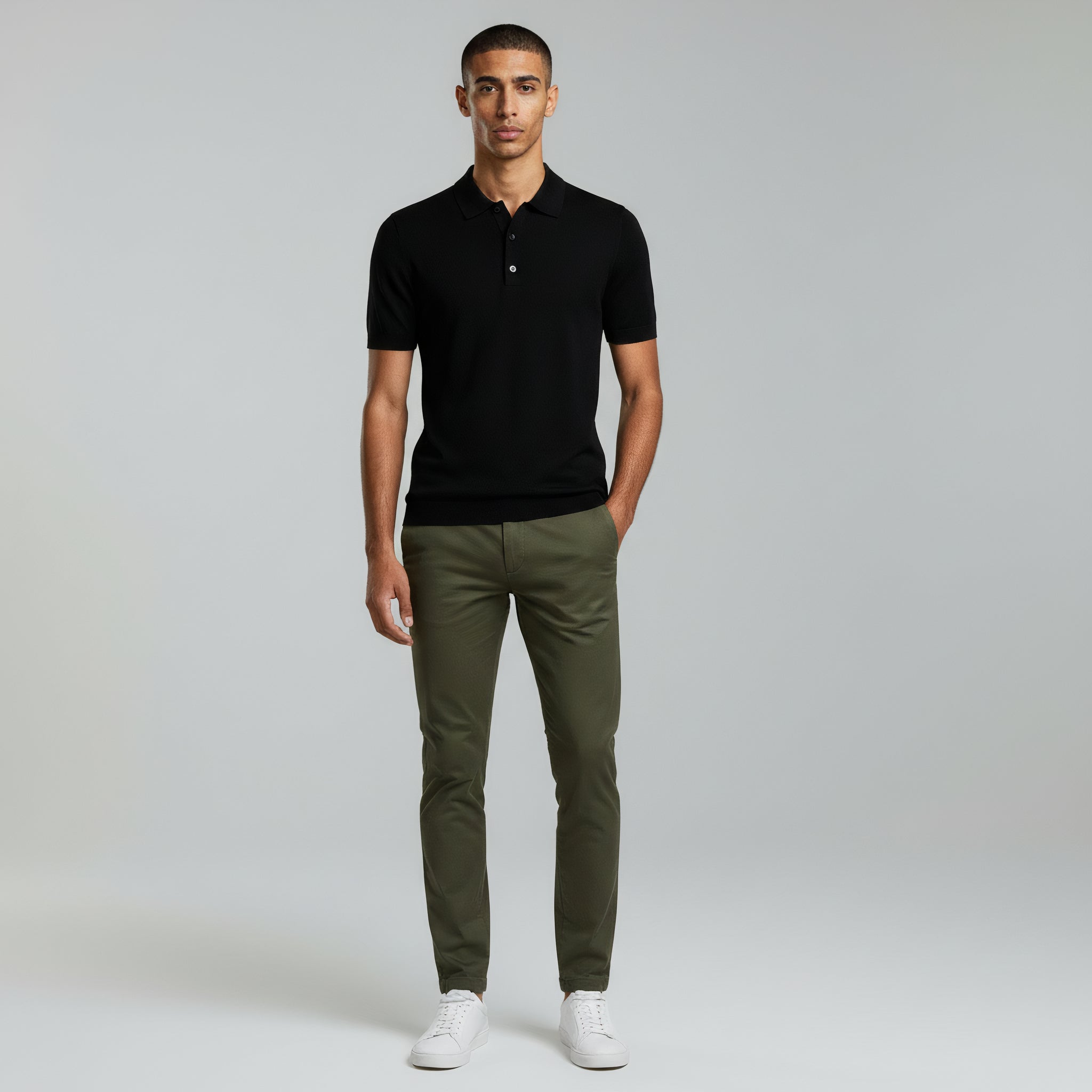 man wearing black polo shirt and green pants on a plain background