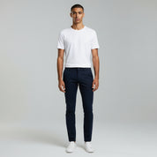 man wearing white shirt top paired with dark blue pants on a plain background