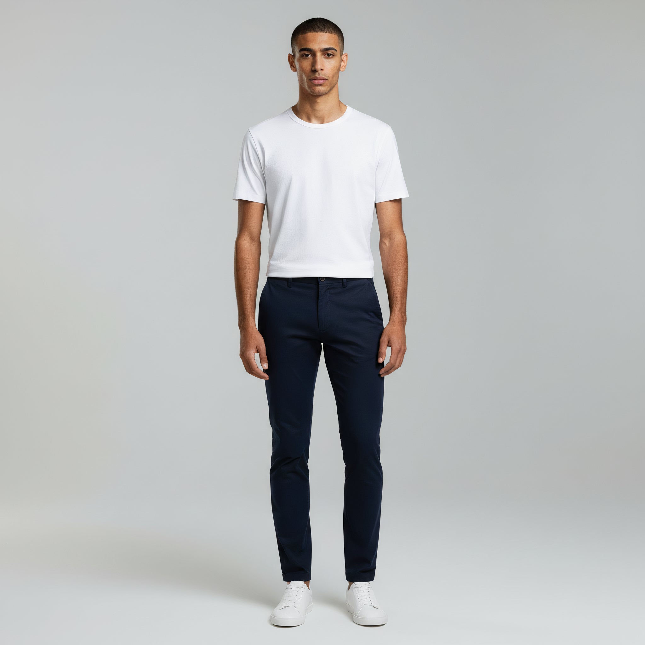 man wearing white shirt top paired with dark blue pants on a plain background