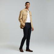 man wearing light brown buttoned jacket with white inner shirt paired with dark grey pants on a plain background