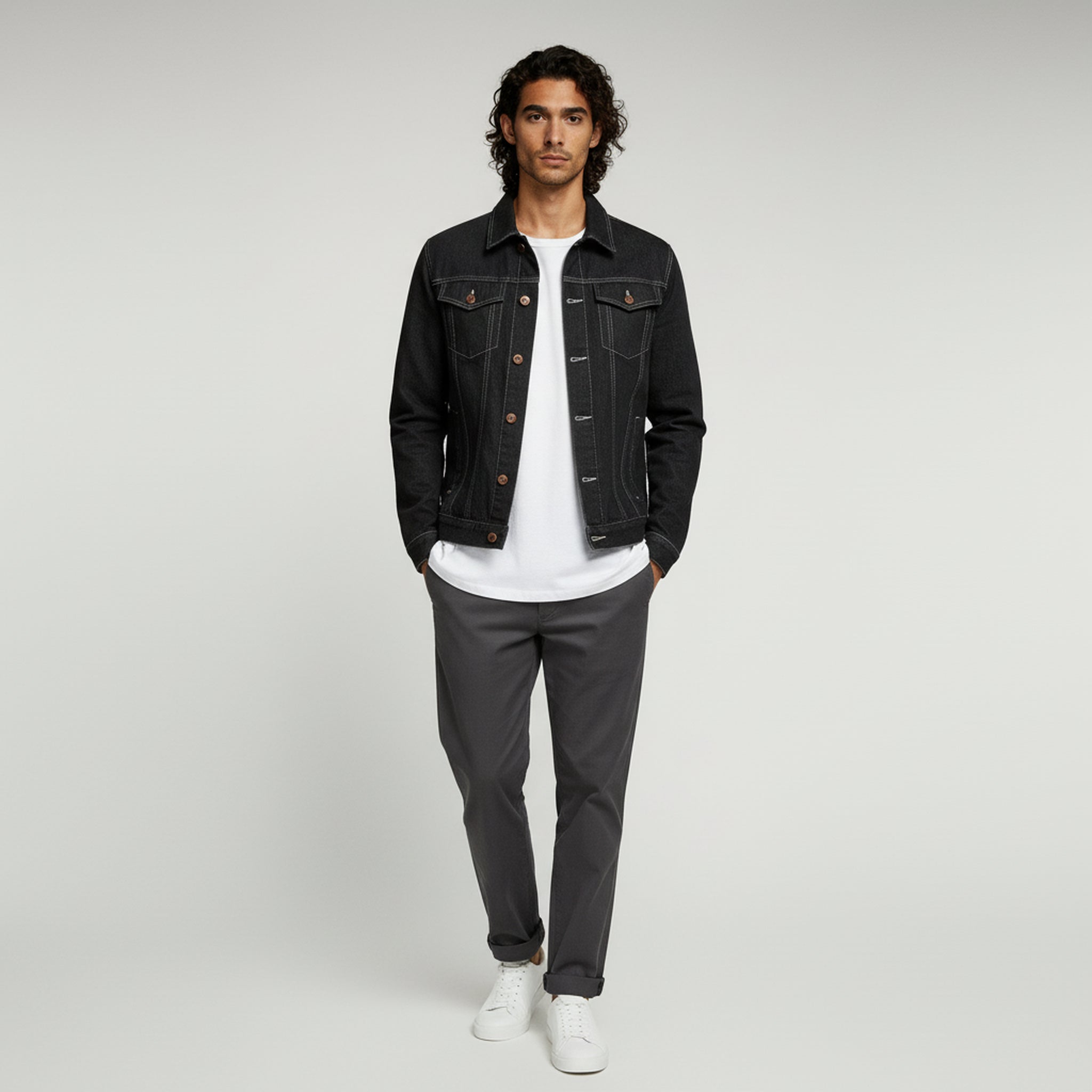 man wearing white shirt with black denim jacket and gray pants on a plain background