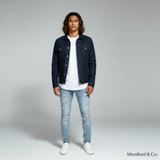 man in white shirt with denim jacket paired with slim fit jeans on a plain background