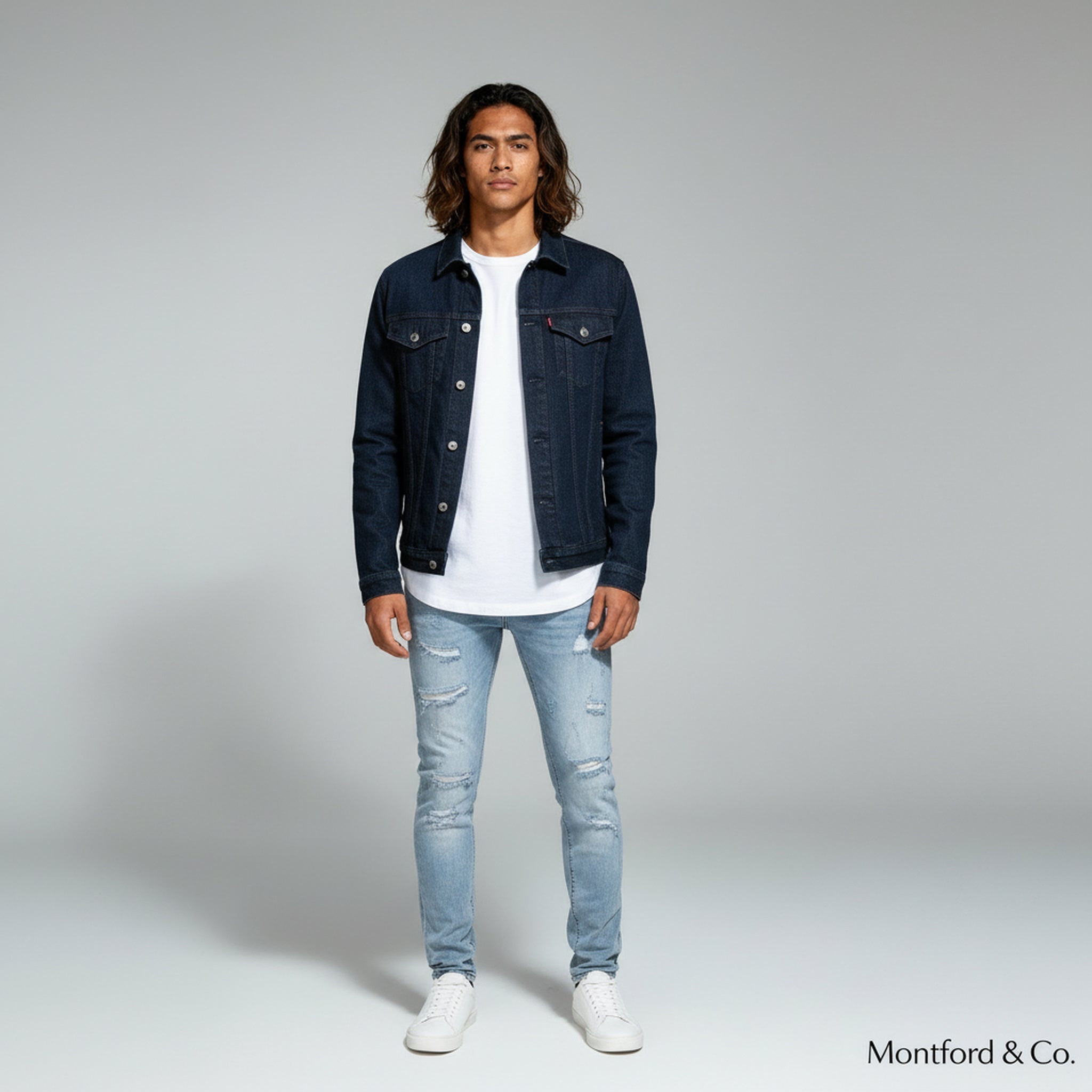 man in white shirt with denim jacket paired with slim fit jeans on a plain background