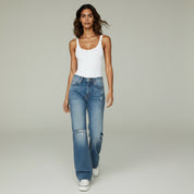lady in white sleeveless top and blue jeans on a plain background