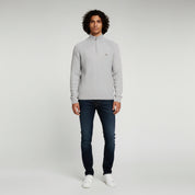 man wearing light gray sweater and black pants on a plain background