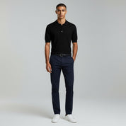 man wearing black polo shirt and navy-blue pants on a plain background