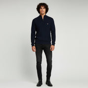 man wearing navy blue sweater and black pants on a plain background