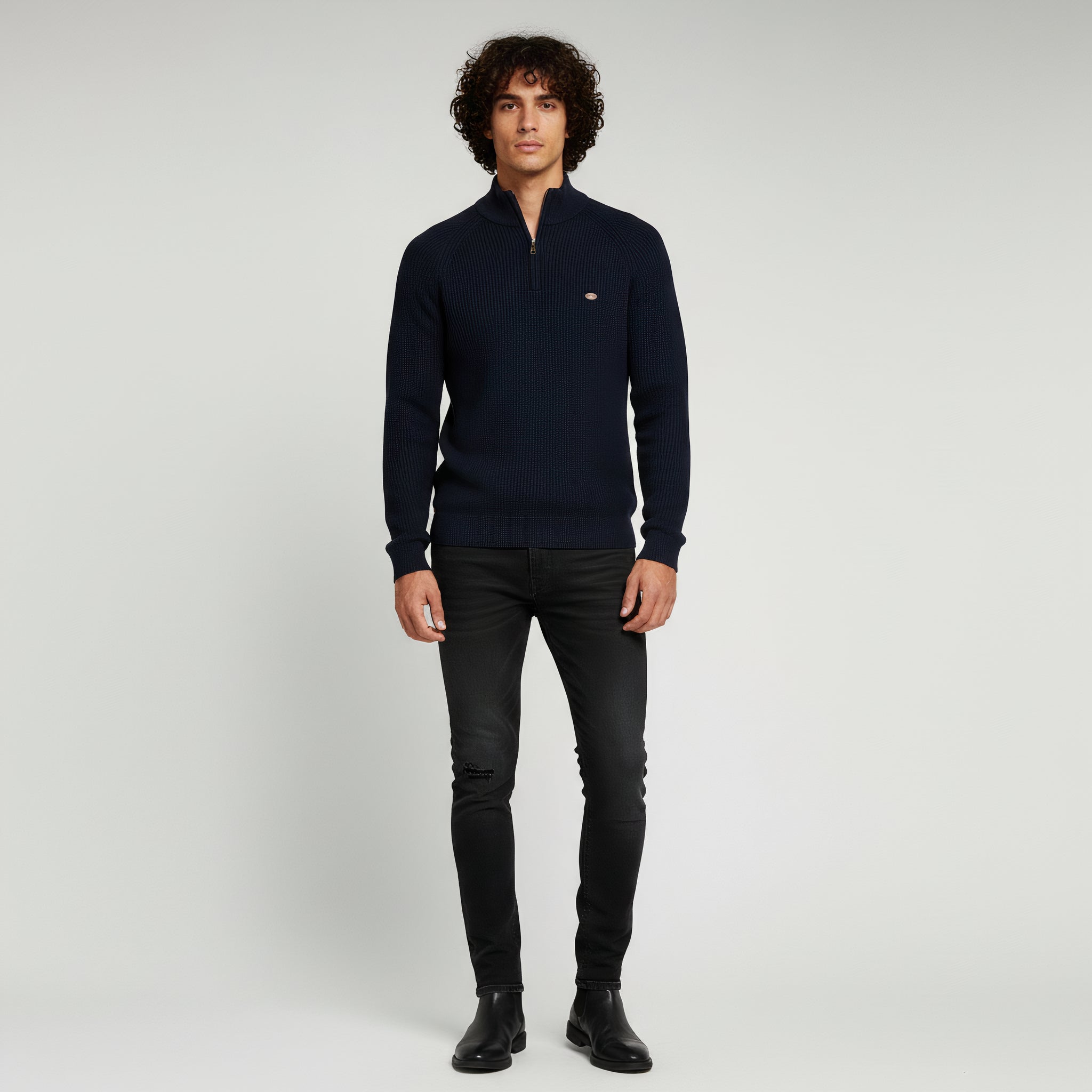 man wearing navy blue sweater and black pants on a plain background