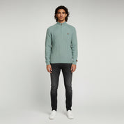 man wearing ocean blue sweater and black pants on a plain background