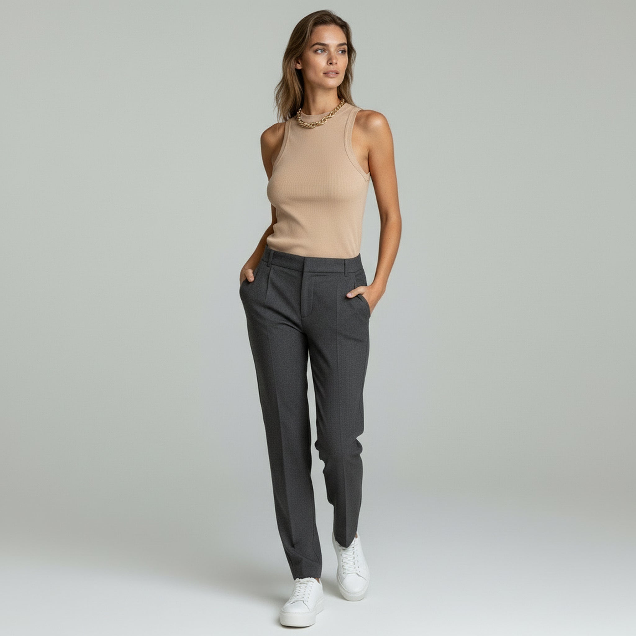 lady in beige top sleeveless knit and grey trousers on a plain background