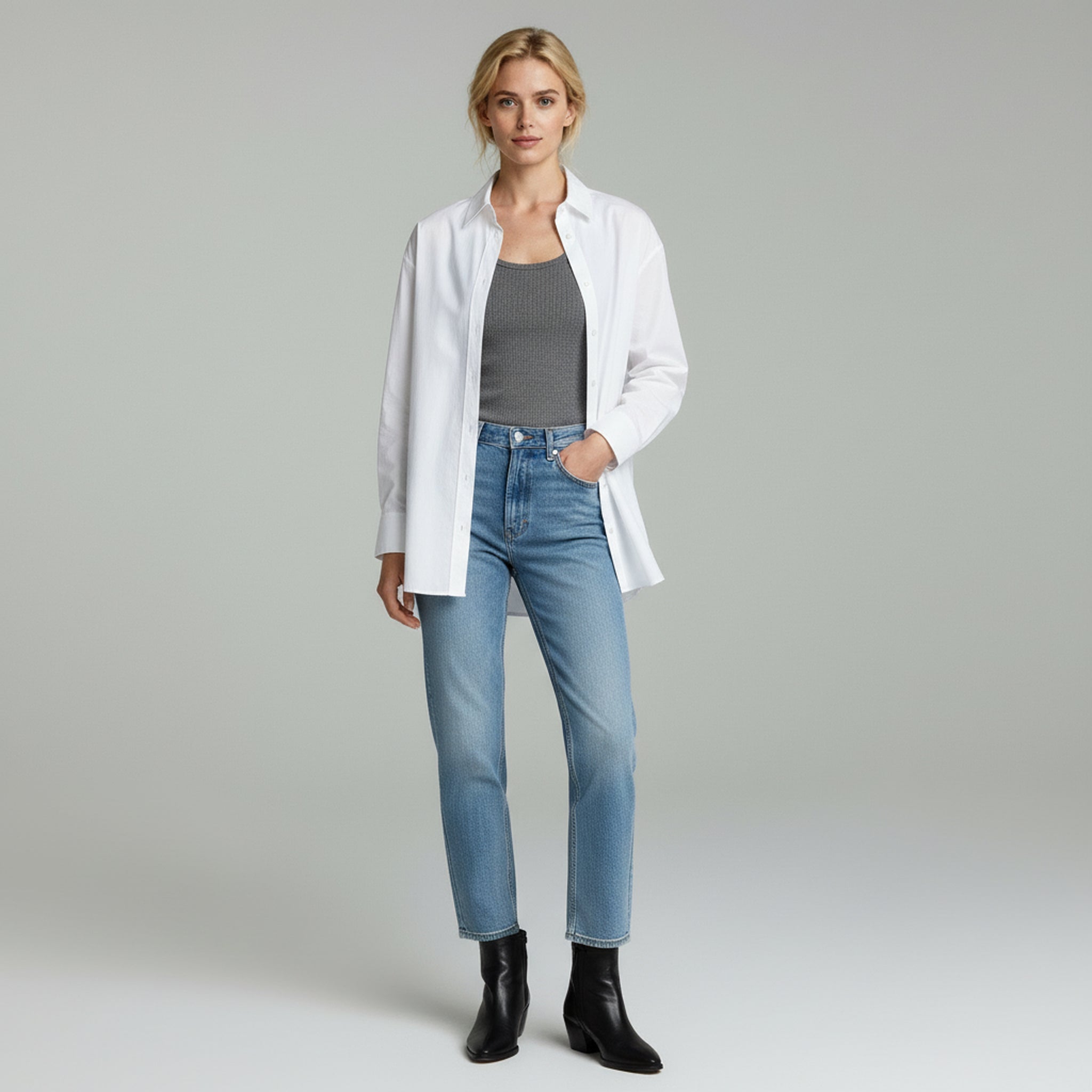 woman wearing grey inner top and white loose long sleeve paired with slim blue jeans on a plain studio background