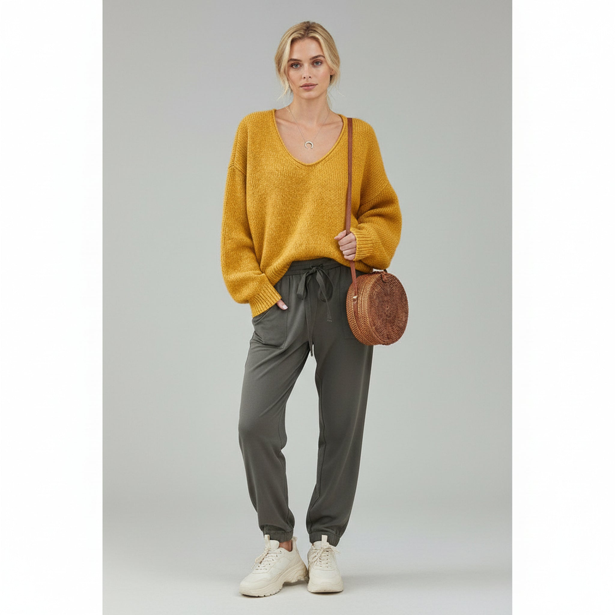 woman wearing orange sweater and grey trousers on a plain background