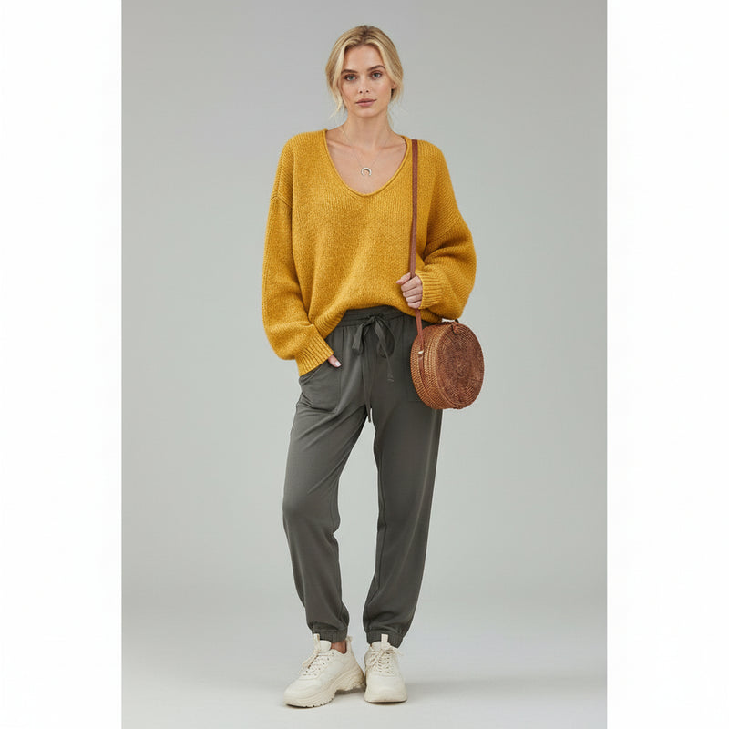 woman wearing orange sweater and grey trousers on a plain background