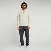 man wearing white sweater and gray pants on a plain background