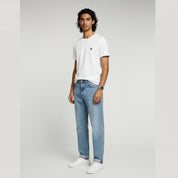 man in white shirt and light blue jeans on a plain background
