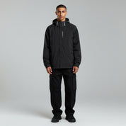 man wearing black waterproof jacket and black cargo pants on a plain background