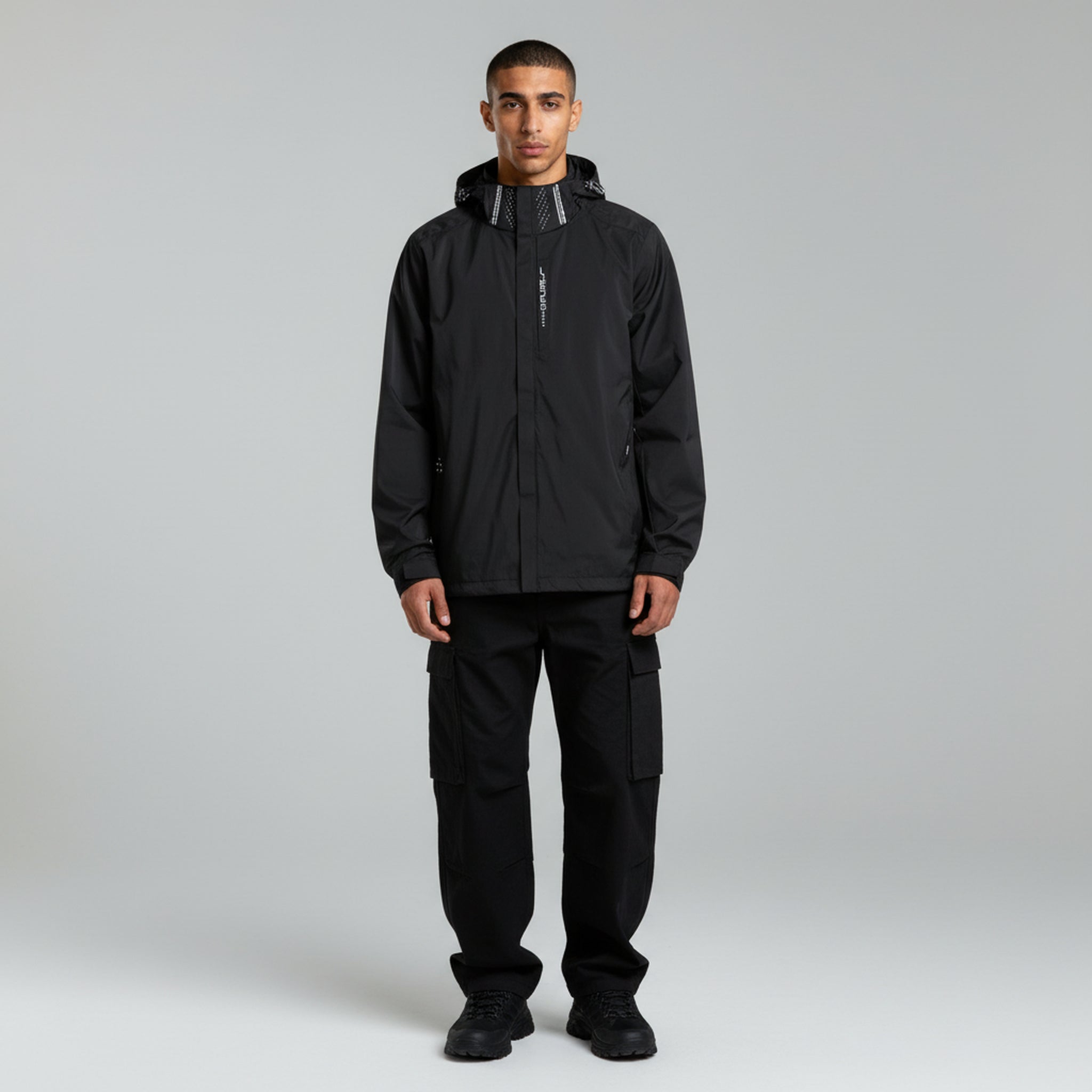 man wearing black waterproof jacket and black cargo pants on a plain background