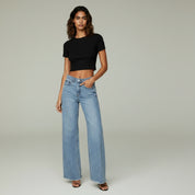 woman wearing black cropped top and wide leg jeans on a plain background