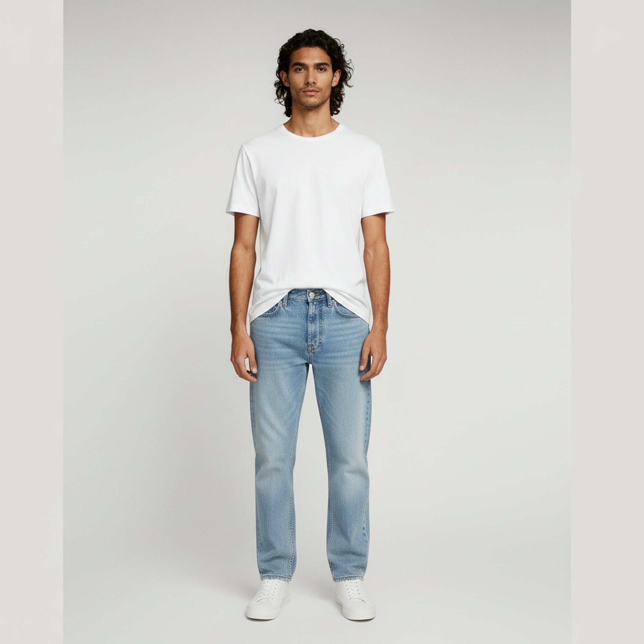 man in white shirt and blue wide leg jeans on a plain background