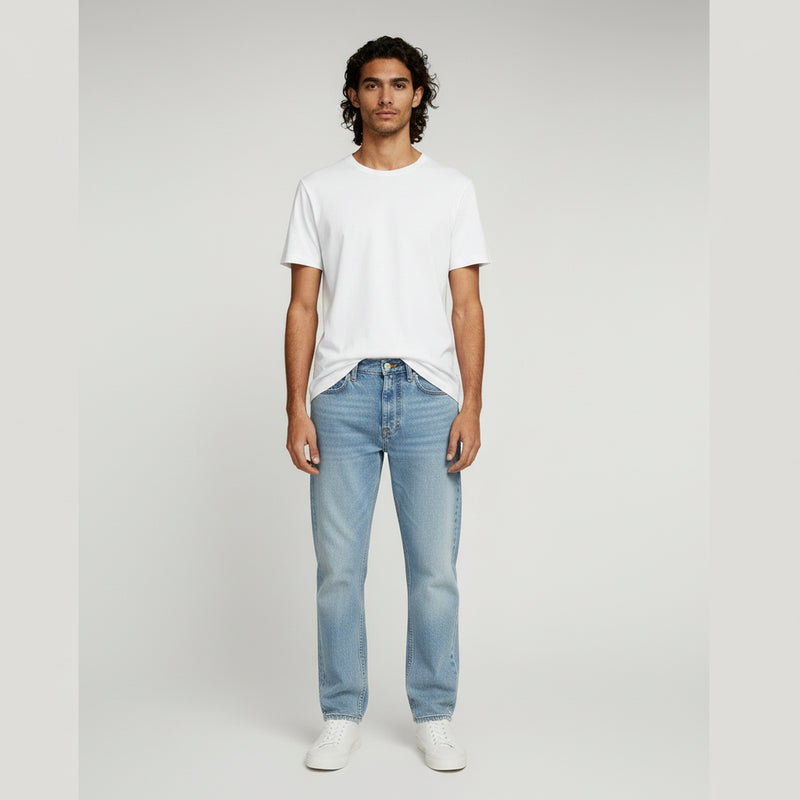 man in white shirt and blue wide leg jeans on a plain background