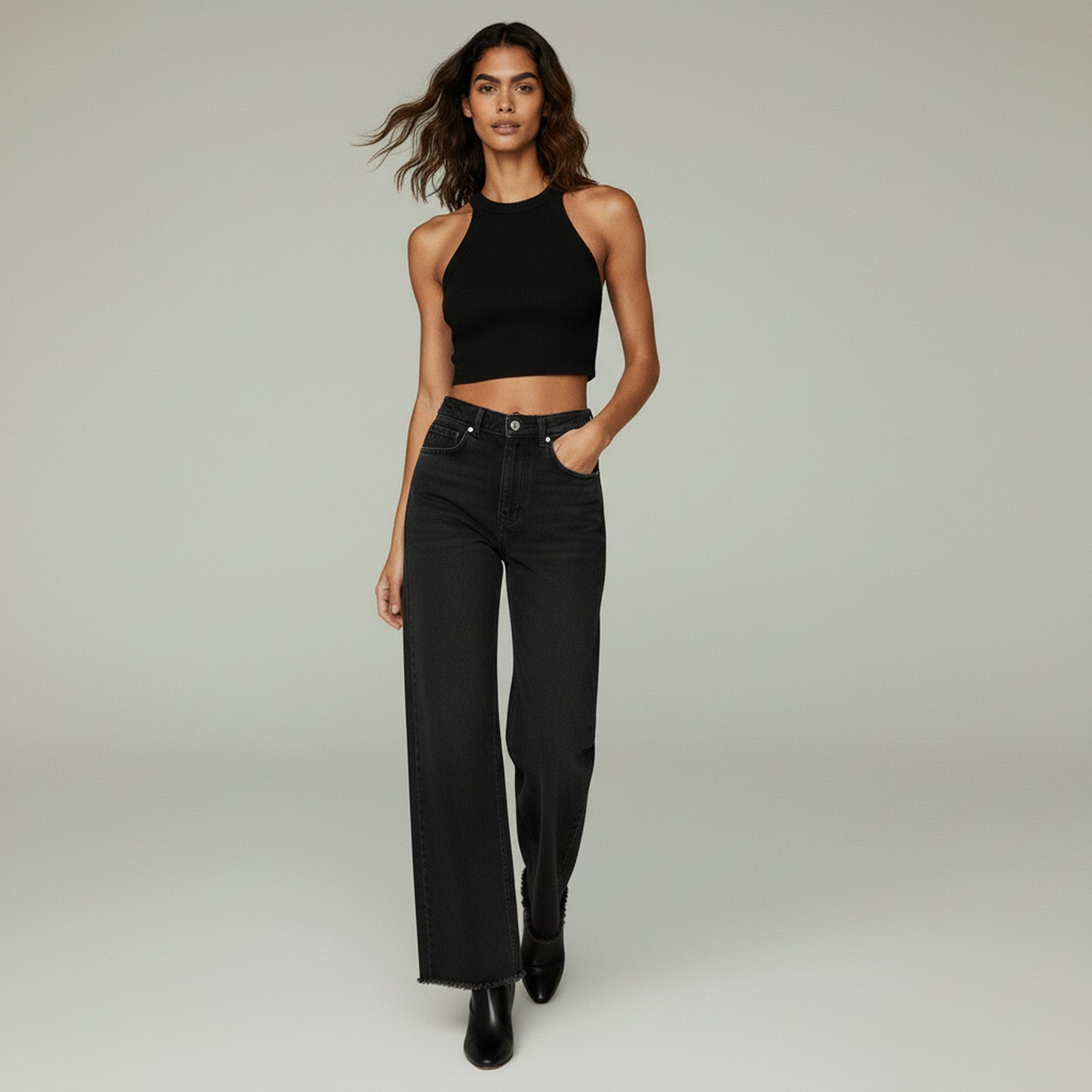 lady in black sleeveless top and black wide leg jeans on a plain background