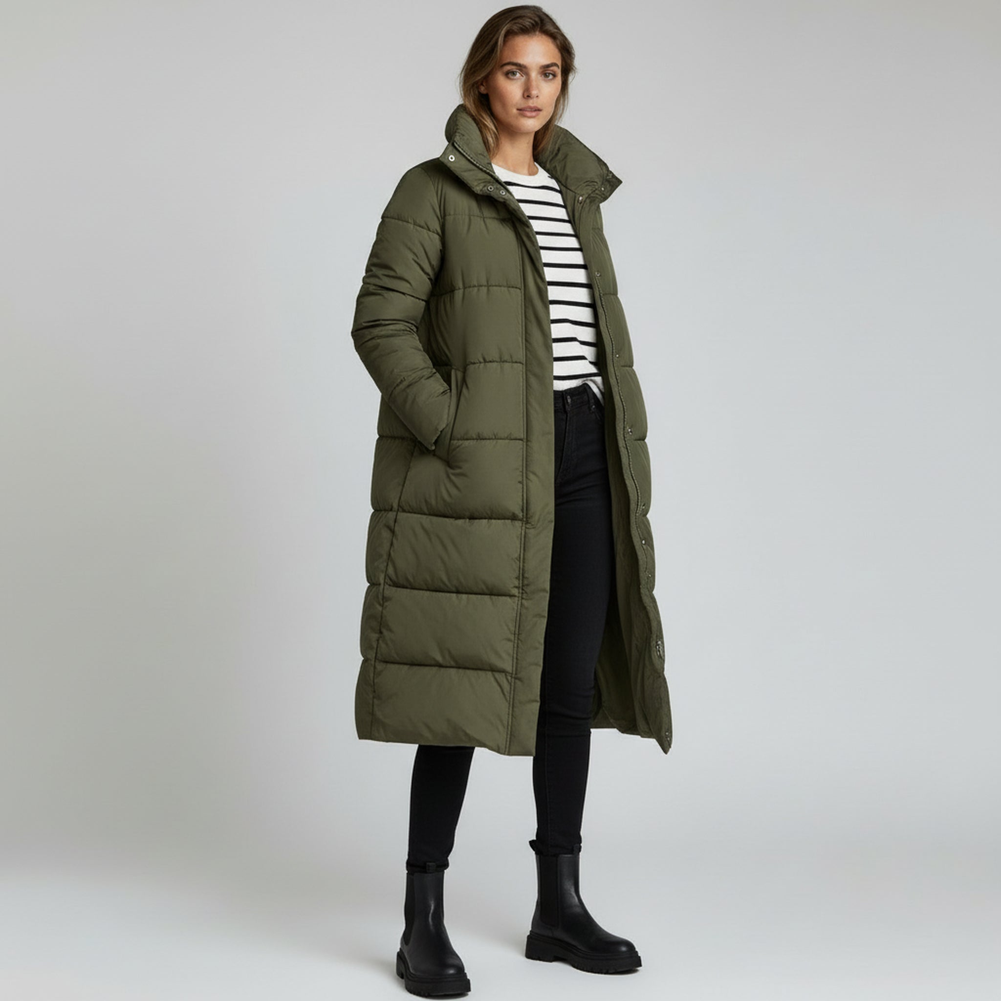 lady wearing green long padded coat and stripe inner top and black pants on a plain background