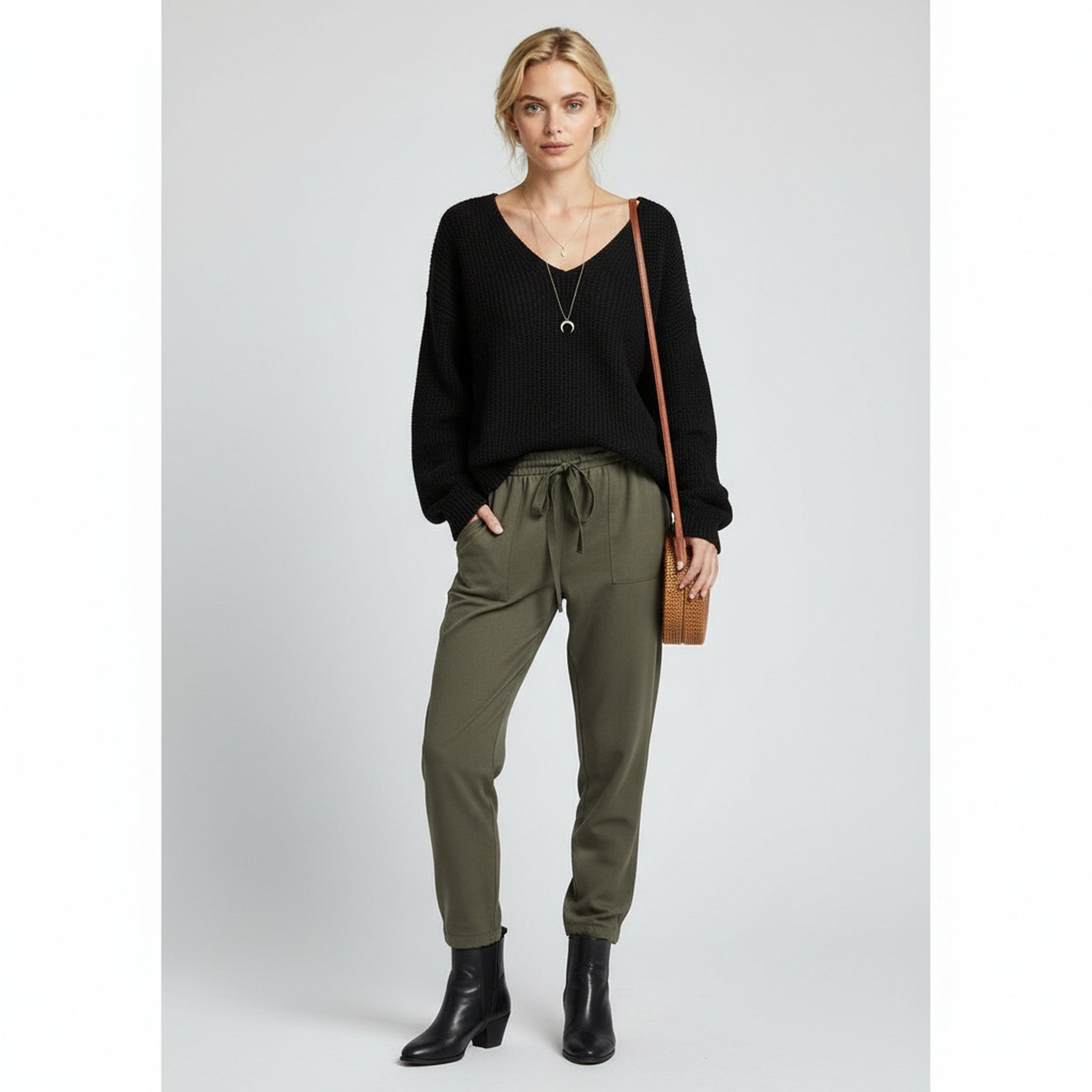 woman wearing black oversized sweater and grey trousers on a plain background