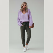 woman wearing purple sweater and black pants on a plain background