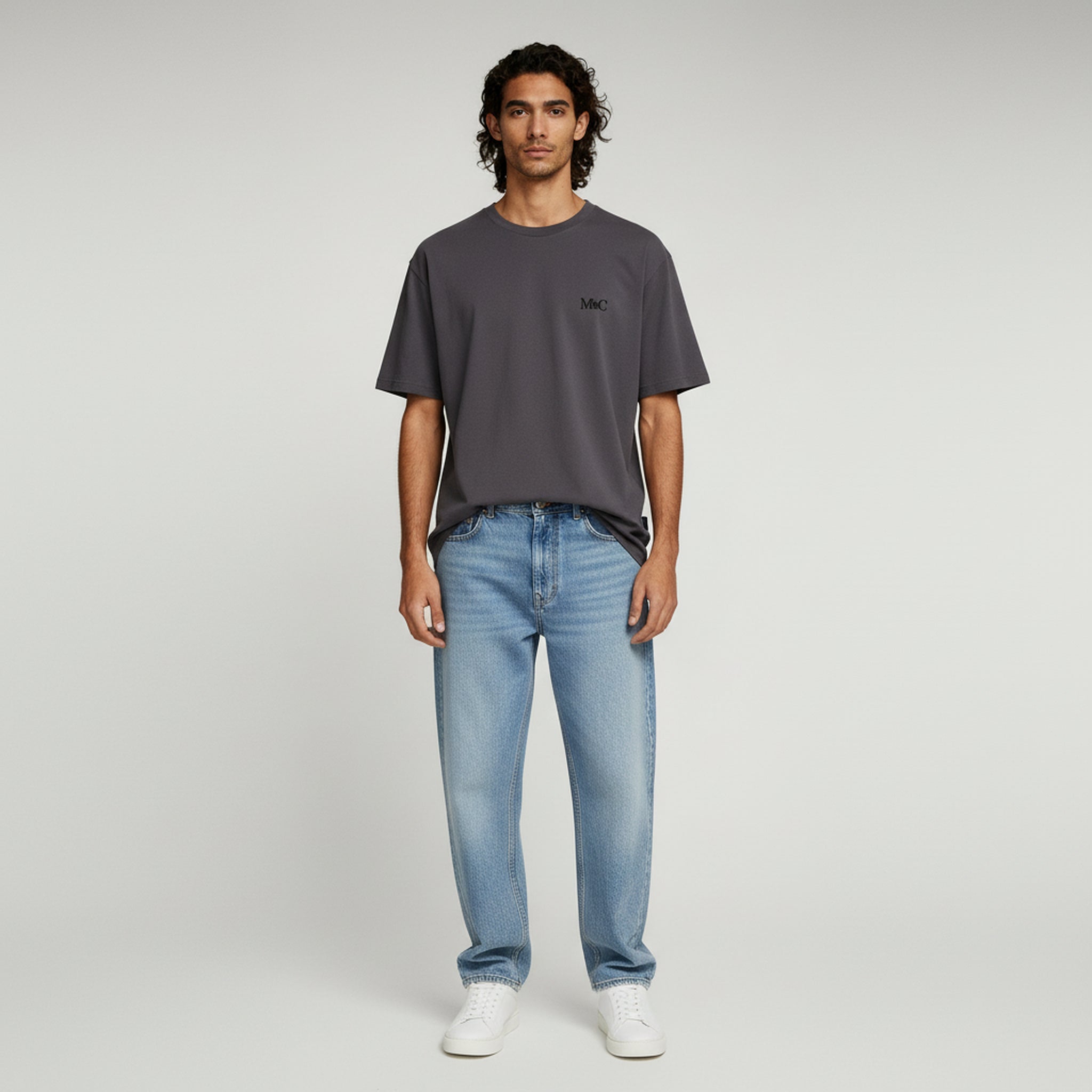 man wearing dark brown shirt and light blue jeans on a plain background