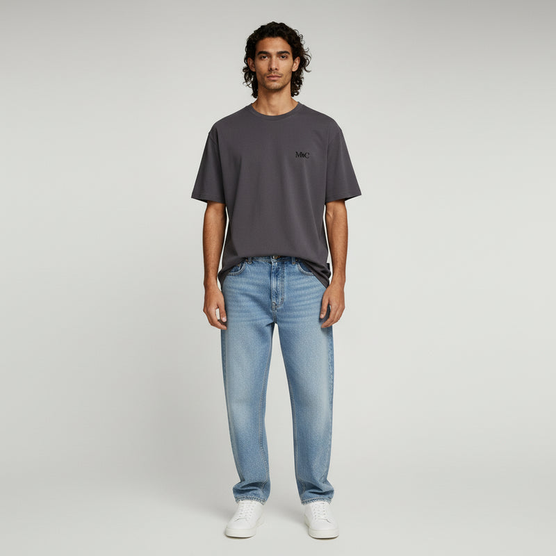 man wearing dark brown shirt and light blue jeans on a plain background