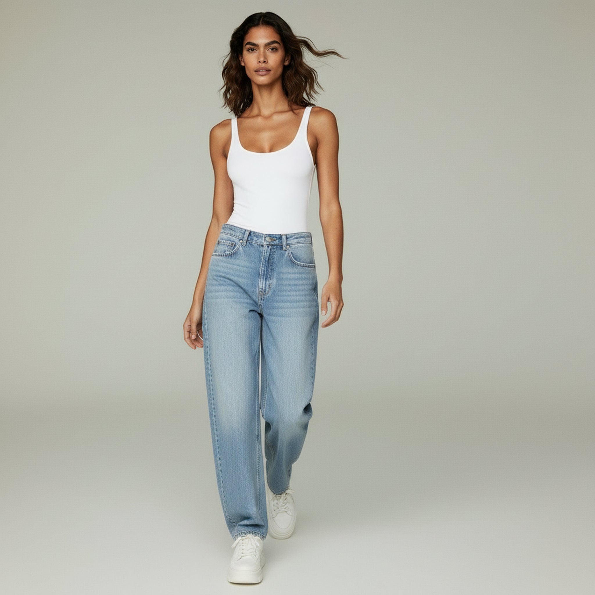 woman wearing white top and blue jeans on a plain background