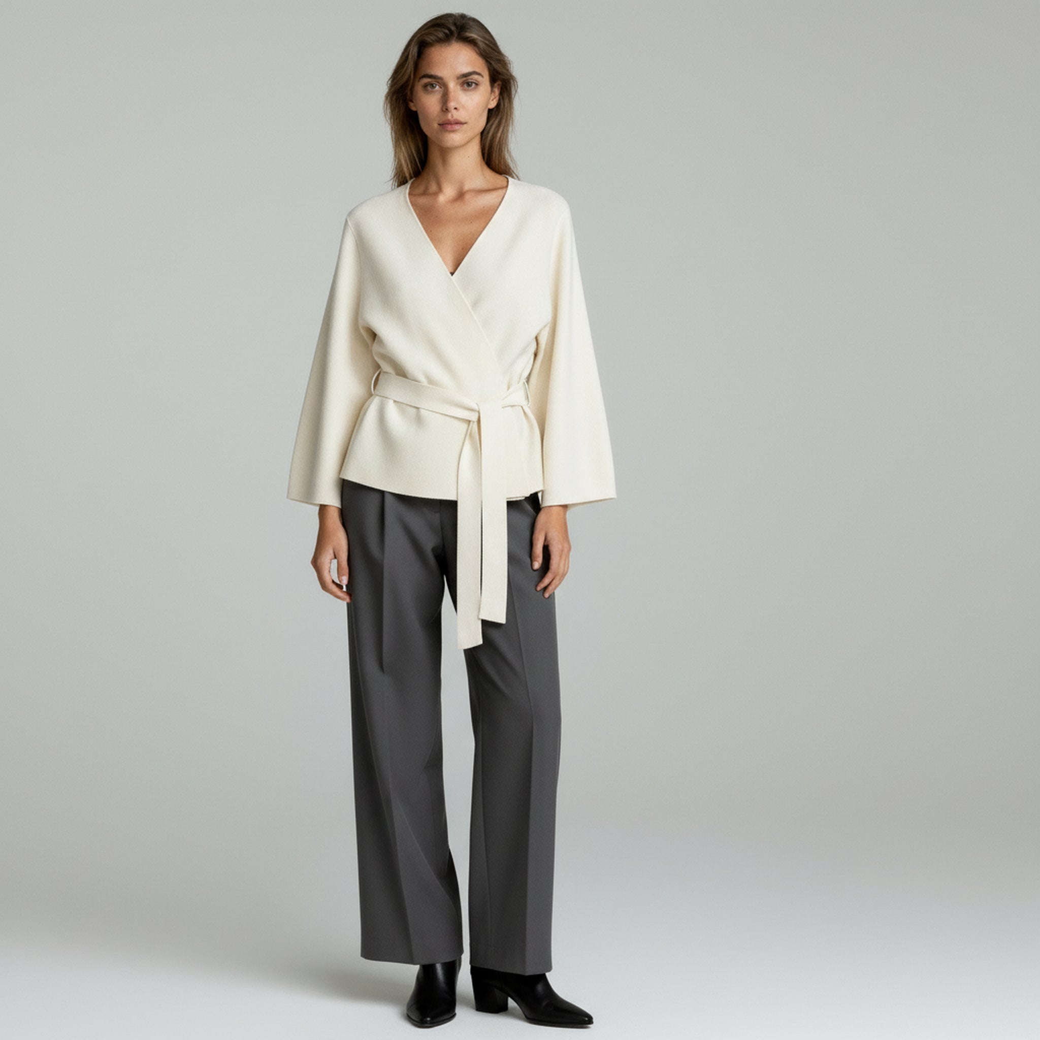 woman wearing white tied blazer and grey trousers on a plain background